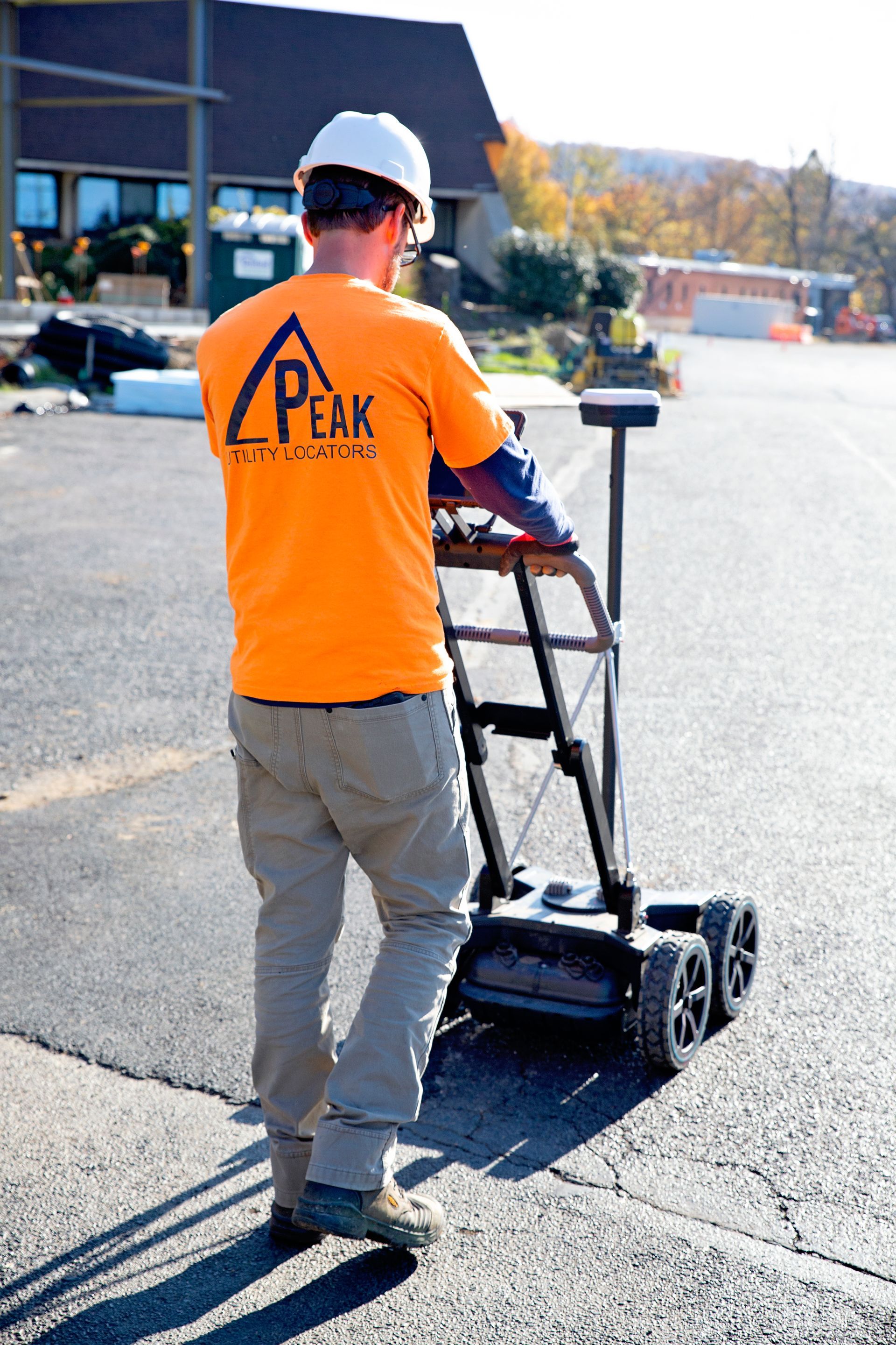 Worker in orange shirt operating a pavement-marking machine in a parking lot.