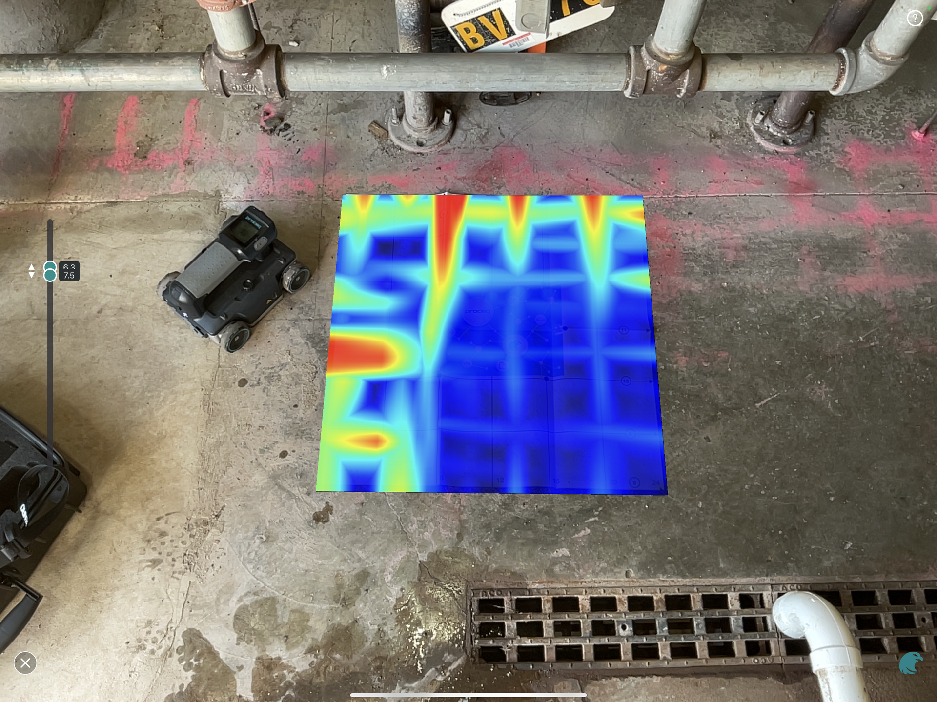 Overhead view of a blue thermal map on concrete beside pipes, a drain, and a black device.