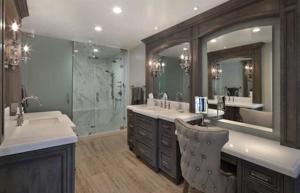 A bathroom with two sinks, wooden cabinets, two mirrors, and a walk in shower
