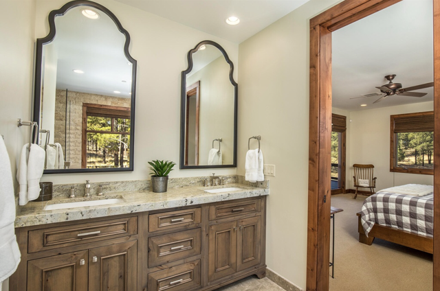 A bathroom with two sinks, cabinets, two mirrors, and a bed