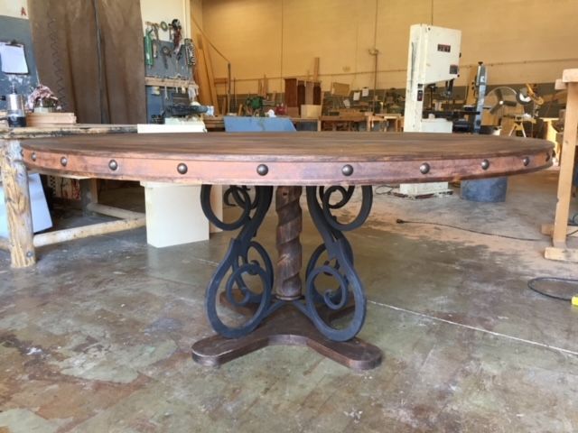 A round wooden dining table with a wrought iron base in a workshop