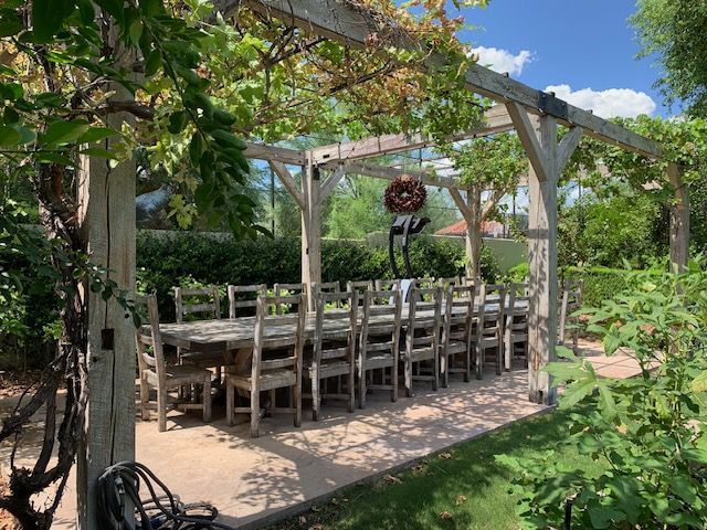A long dining table and chairs under a pergola in a garden