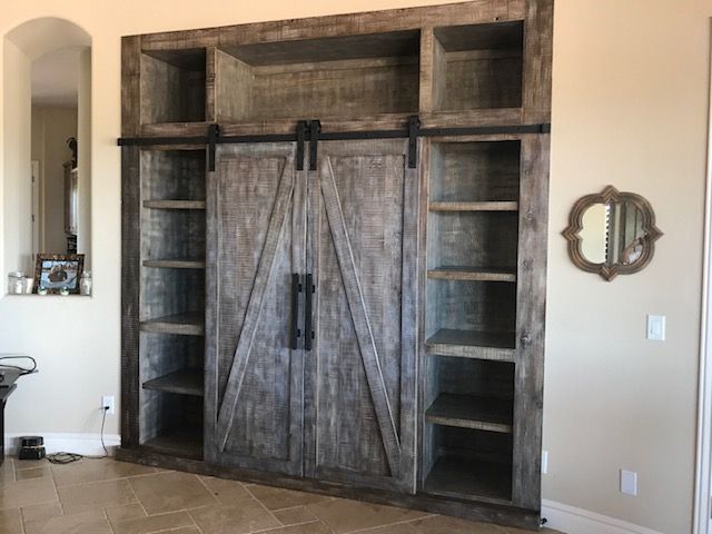A large wooden cabinet with sliding barn doors and shelves in a living room
