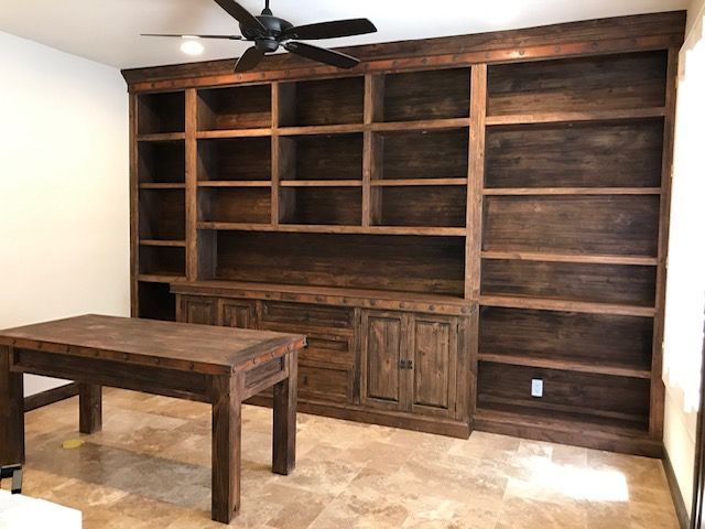 A home office room with a table and shelves and a ceiling fan