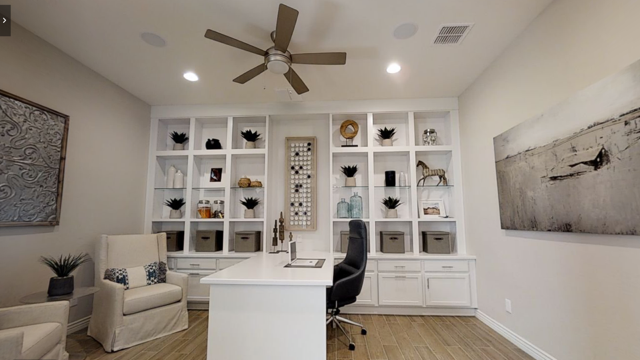 A white home office room with a table and shelves and a ceiling fan