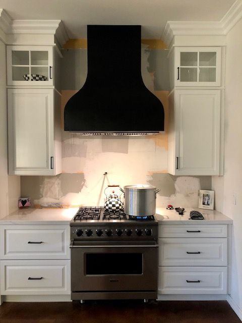 A kitchen with white cabinets and a stove with a black hood