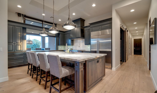 A kitchen with a large island, gray cabinets, and stools