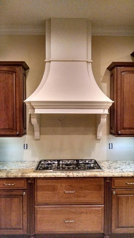 A kitchen with a stove top oven, a hood above it, and wooden cabinets