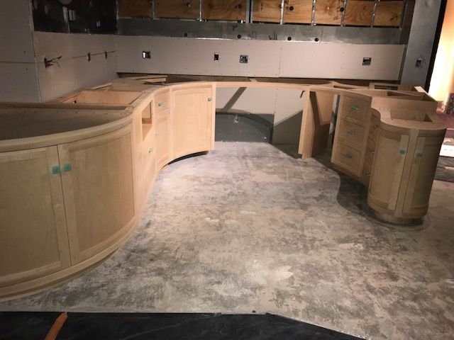 A kitchen under construction with curved cabinets and a concrete floor