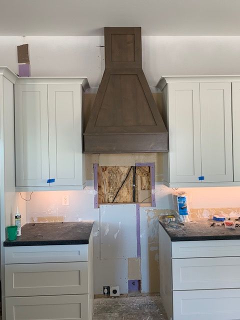 A kitchen with white cabinets and a hood above the stove