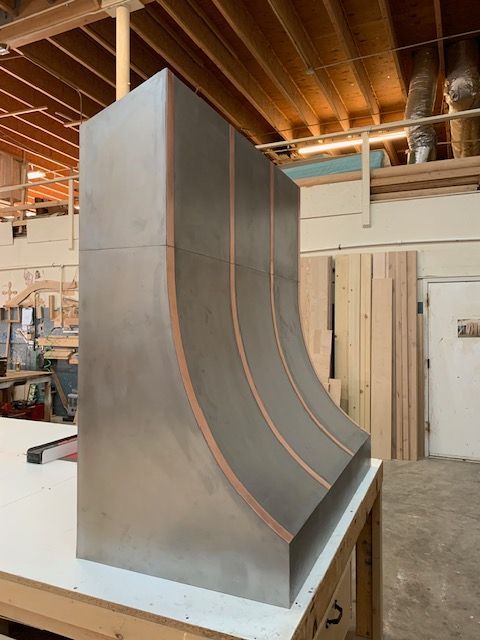 A stainless steel kitchen range hood is sitting on a table in a work shop