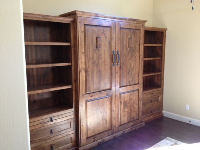A room with a wooden Murphy bed with shelves