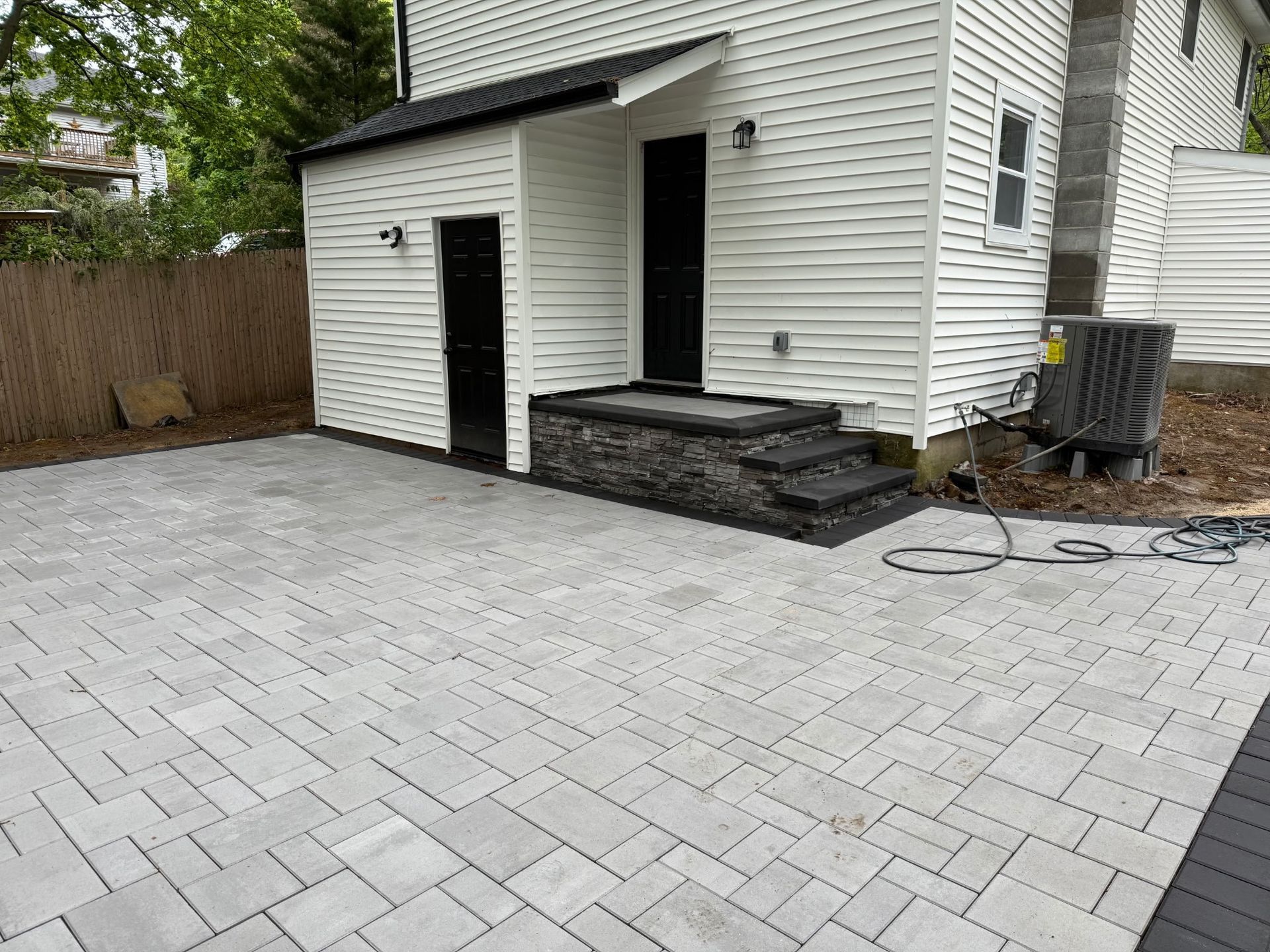 Backyard with light gray paver patio and white house side entry with wooden steps