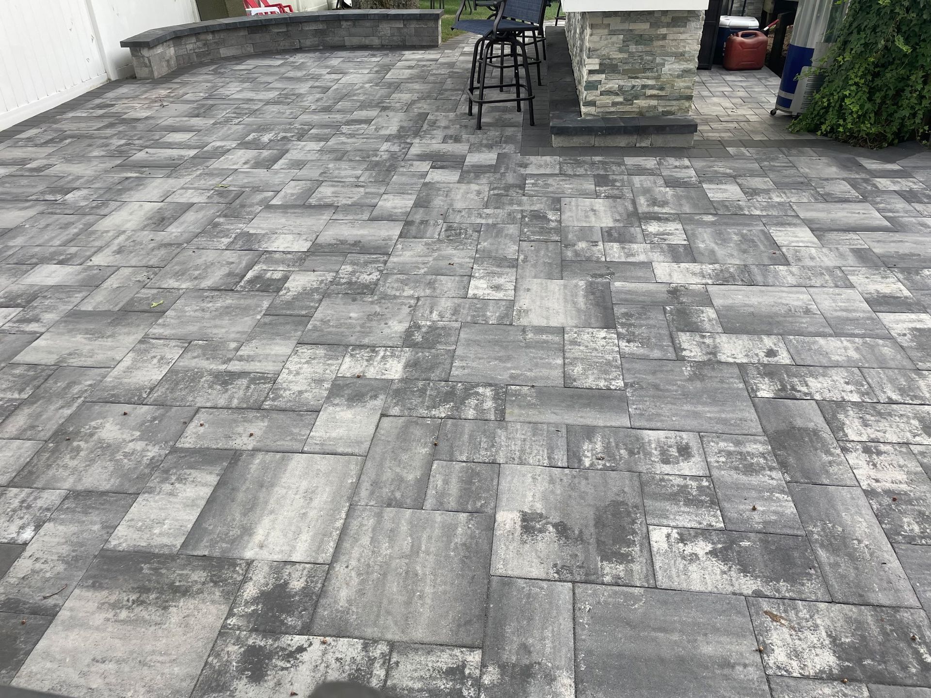 Gray stone patio with patterned pavers, a chair, and a small table near a landscaped yard.