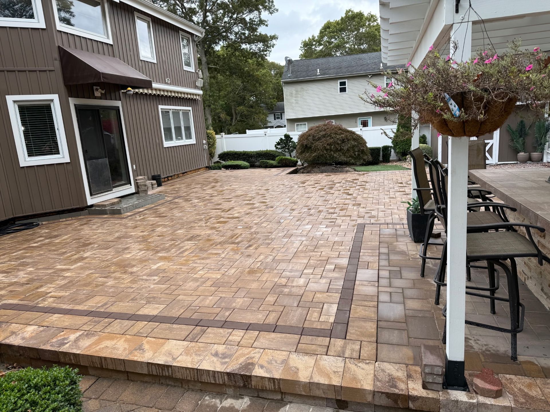 Stone-paved backyard patio between houses, with outdoor furniture and hanging plants.