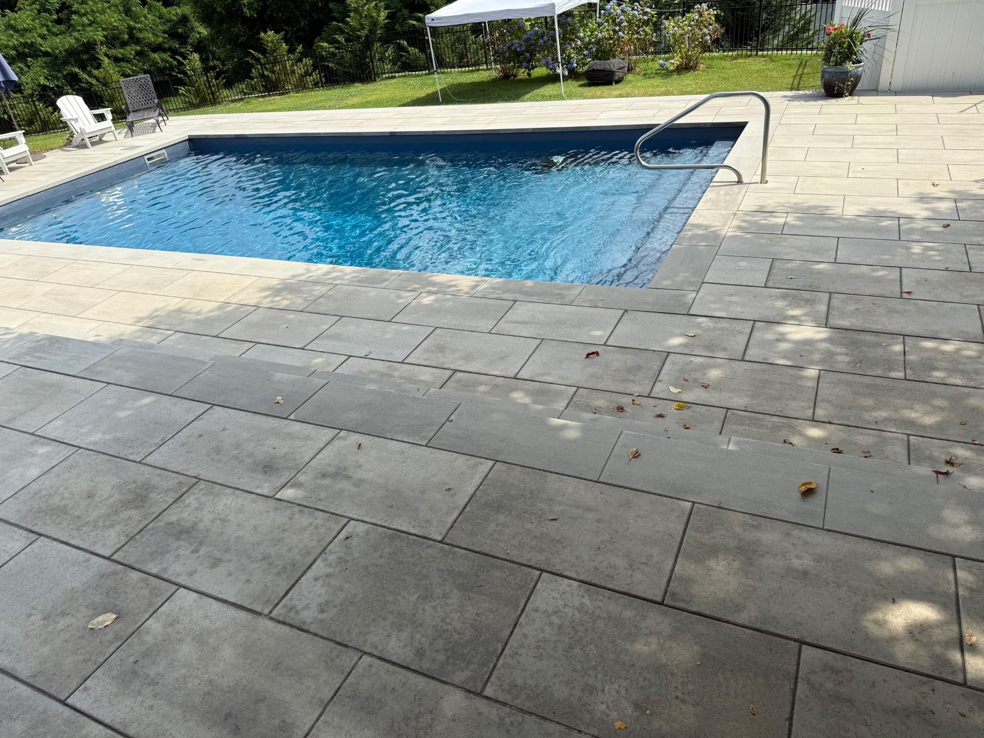 Backyard swimming pool beside a gray stone patio with a curved metal handrail.