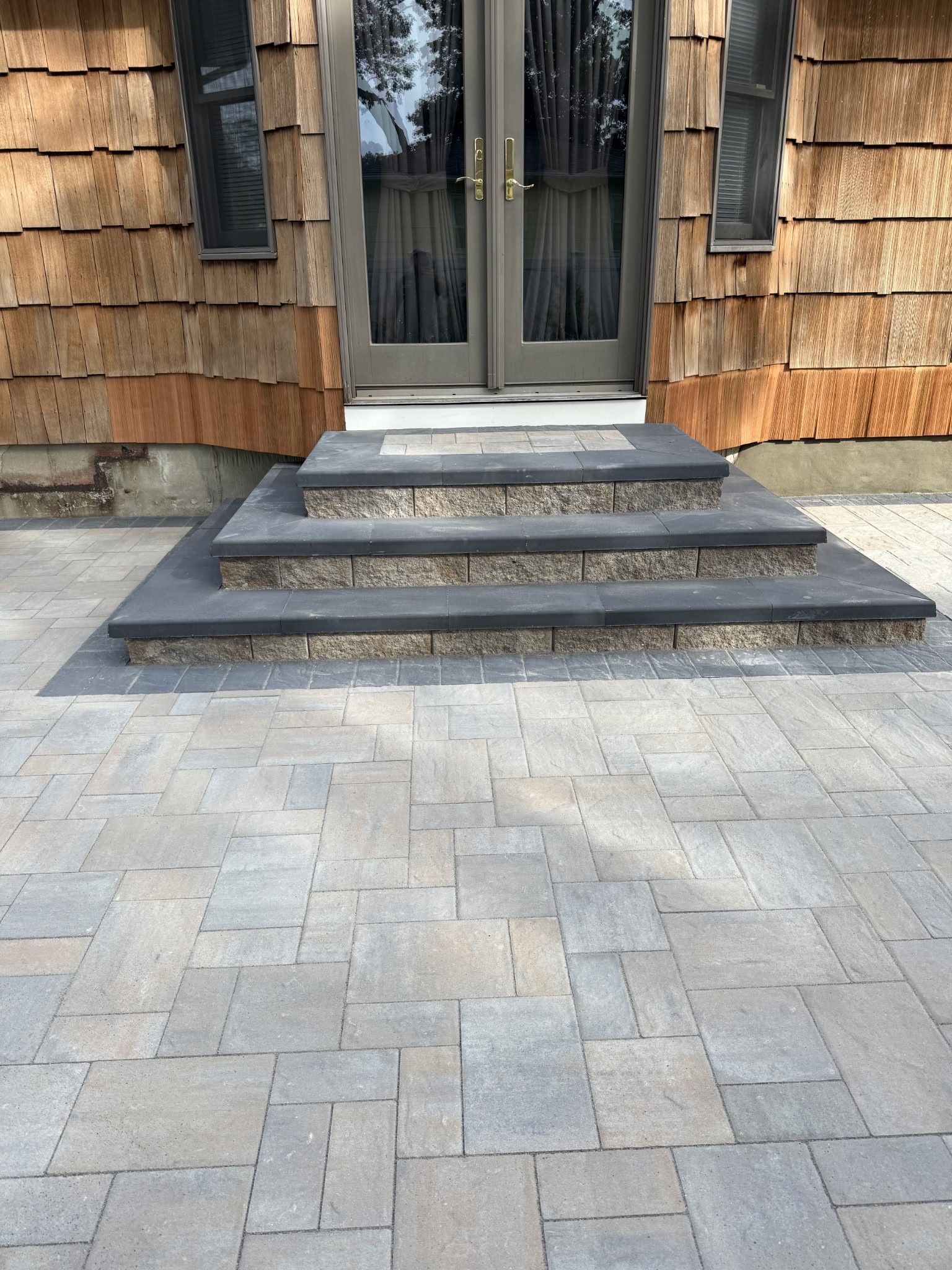 Front entrance with gray stone steps, paved walkway, and double glass doors on a wood-shingled house
