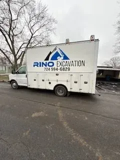 White Rino Excavation truck parked on asphalt. It has storage compartments and logo with contact info.
