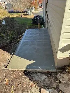 Freshly poured concrete patio next to a house with dirt and grass in the background.