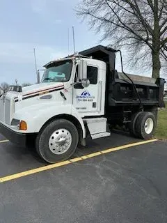White dump truck parked on asphalt, near a tree, with logo on the door.
