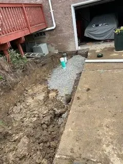 Trench filled with gravel next to a concrete patio and building. A green pipe is visible.