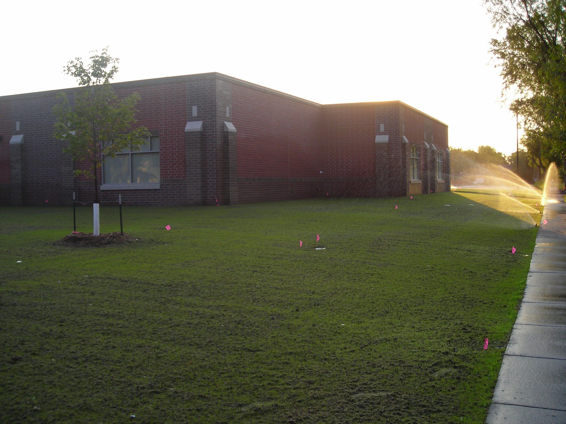 A sprinkler is spraying water on a lush green lawn in front of a building