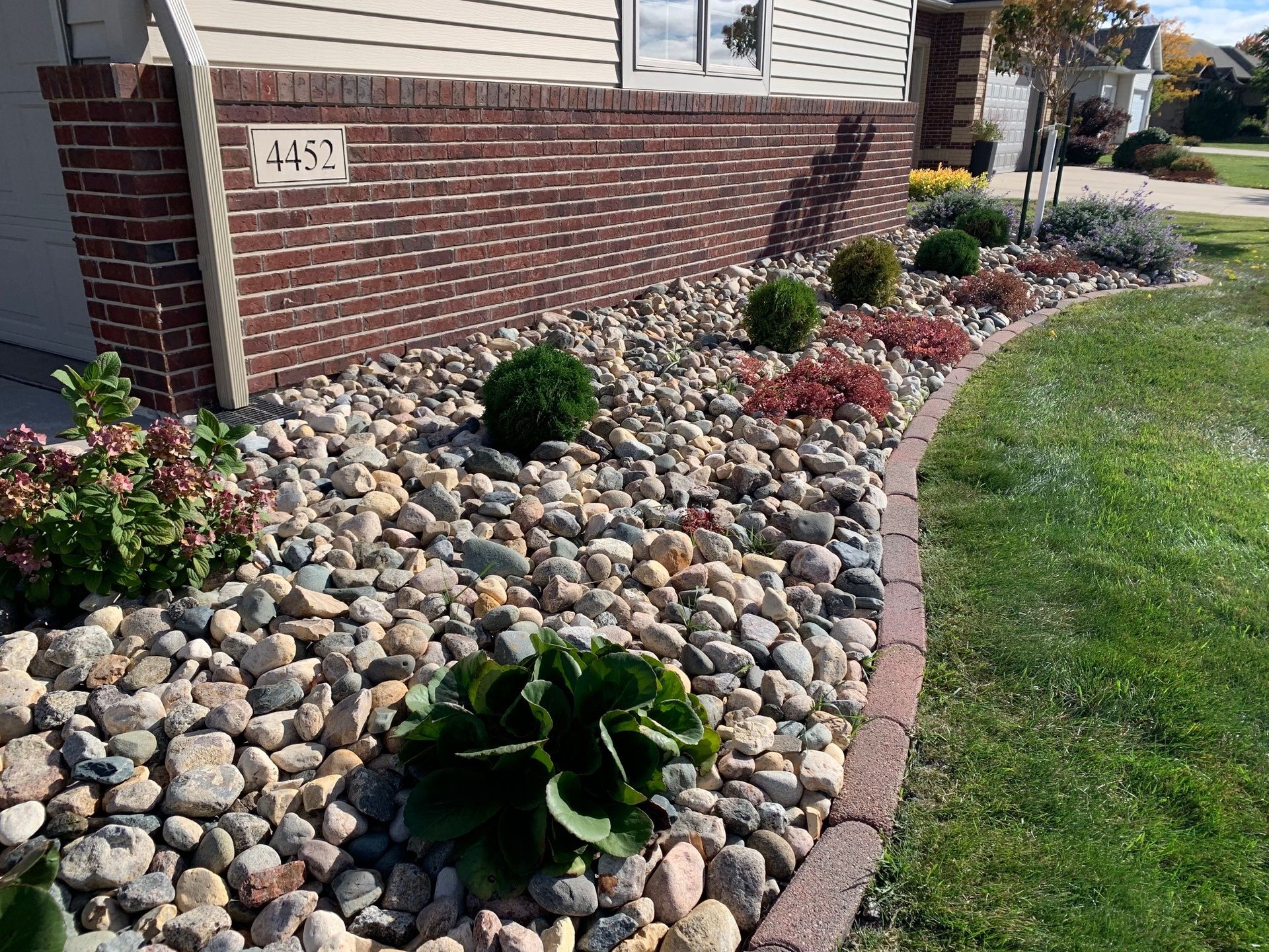 A garden with rocks and plants in front of a brick house.
