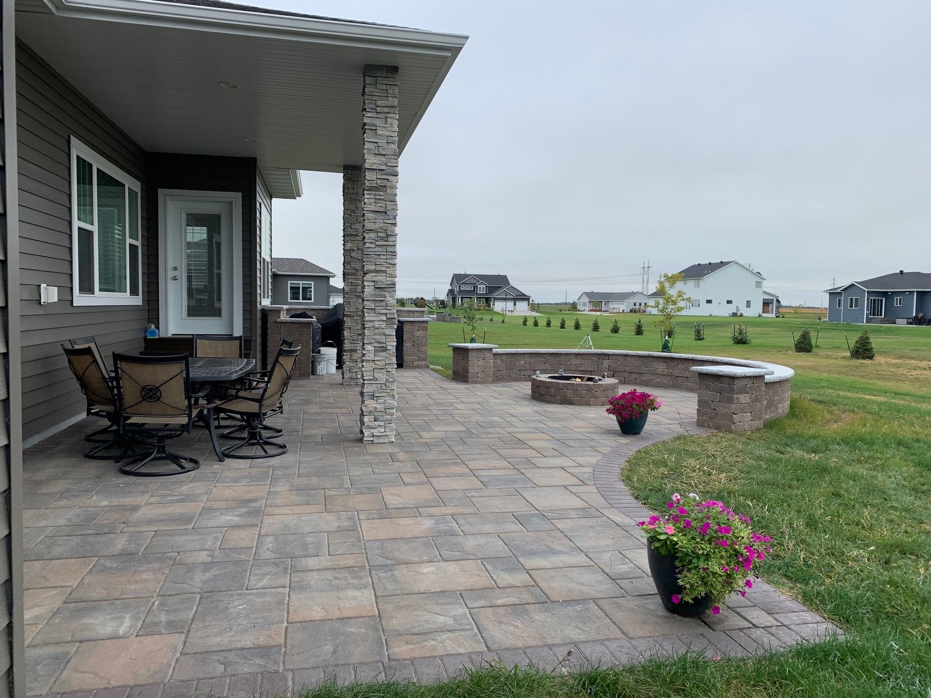 A patio with a table and chairs and a fire pit in front of a house.