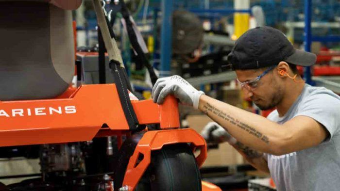 A man is working on a lawn mower in a factory.