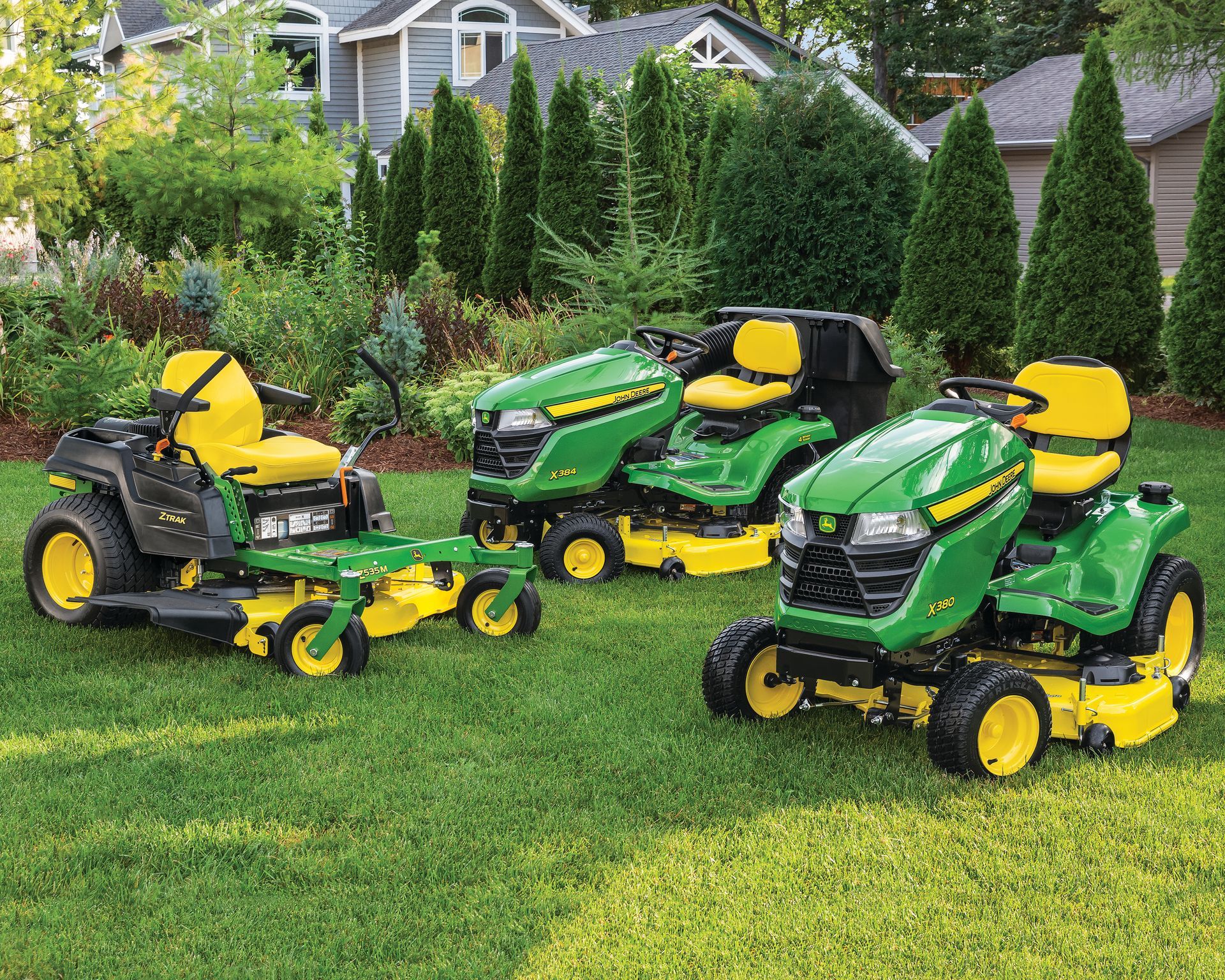 Three john deere lawn mowers are parked on a lush green lawn.