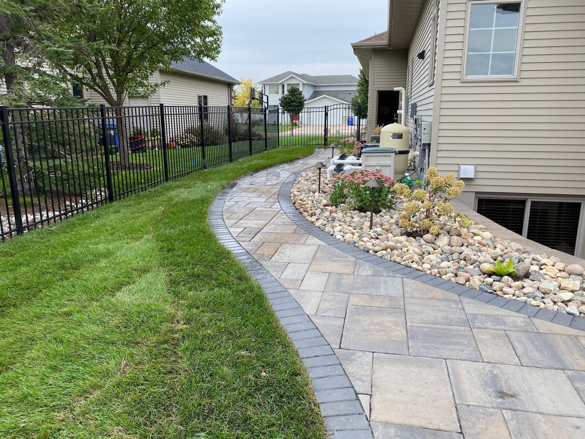 A brick walkway leading to a house with a fence in the background.