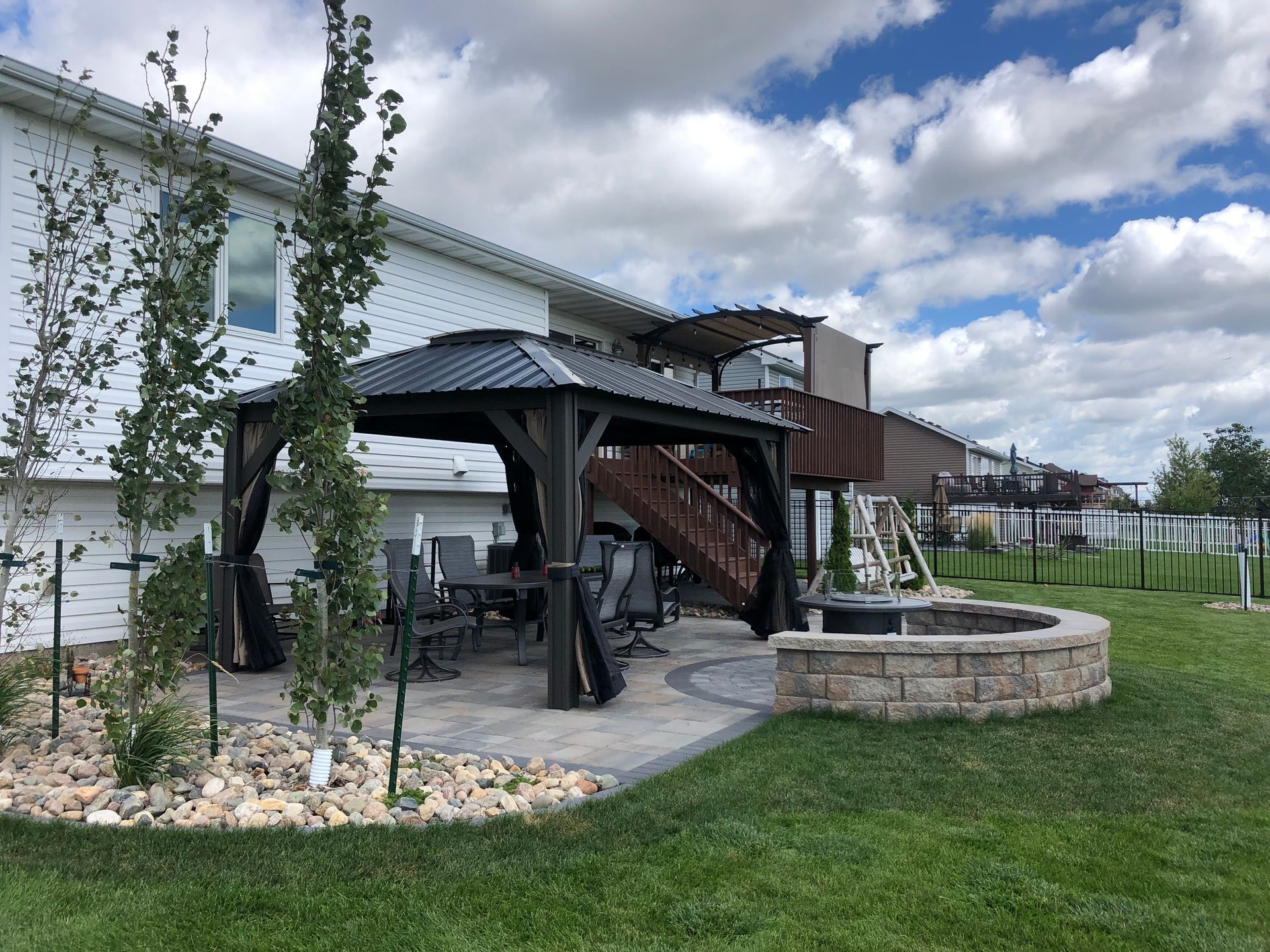 A gazebo is in the backyard of a house next to a fire pit.