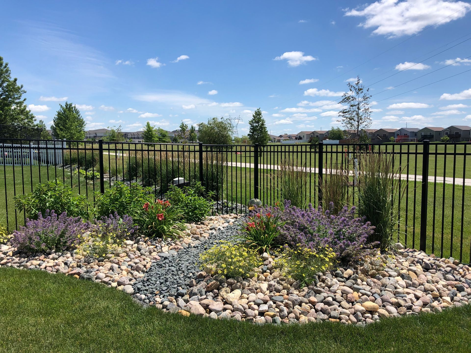 A garden with flowers and rocks in front of a fence.
