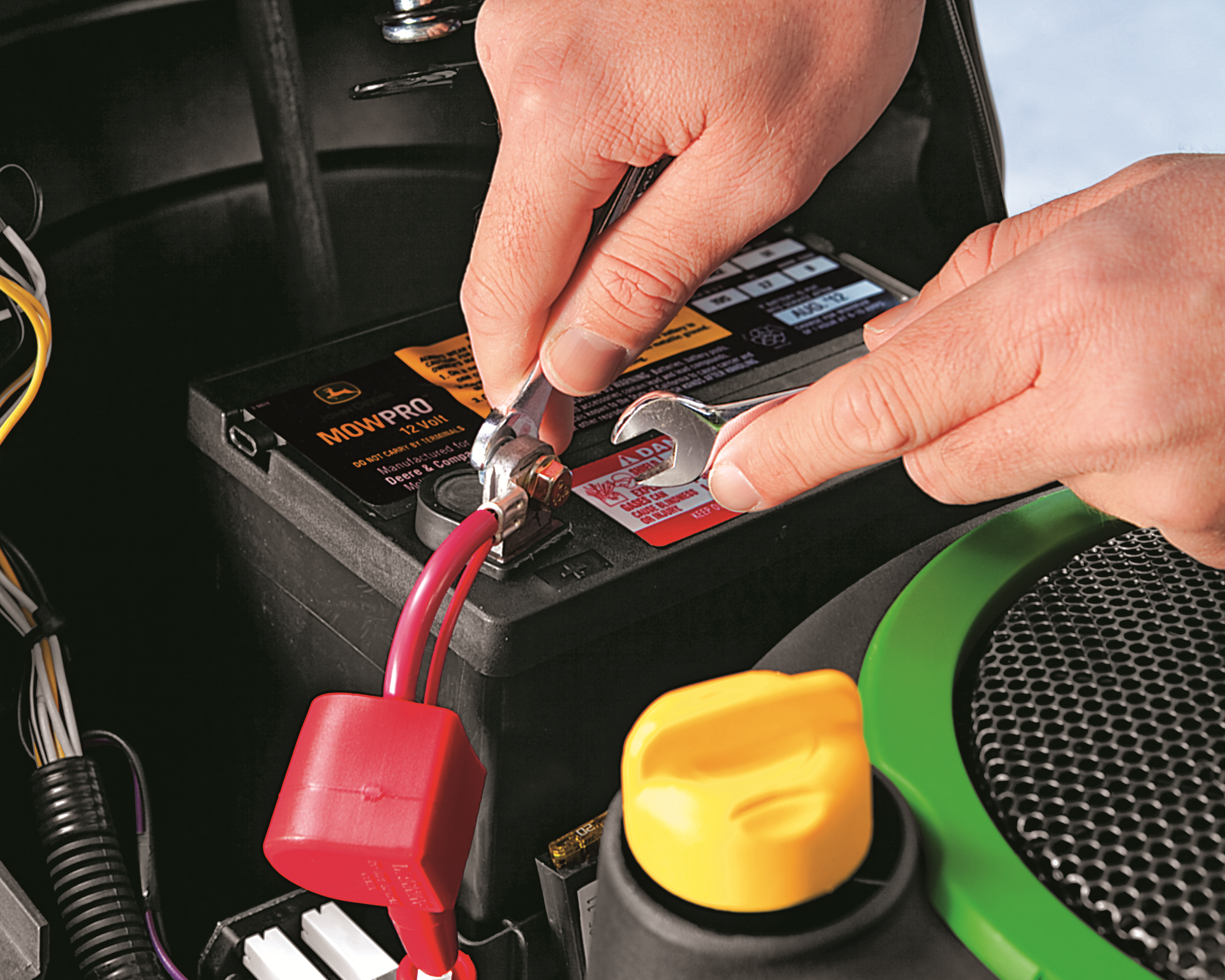 A person is fixing a lawn mower battery with a wrench