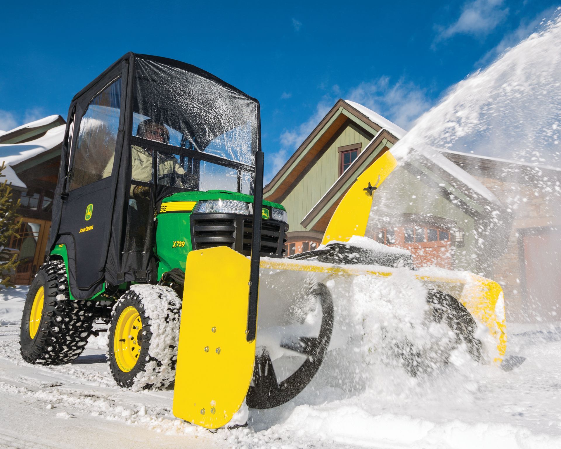 A john deere snow blower is blowing snow in front of a house