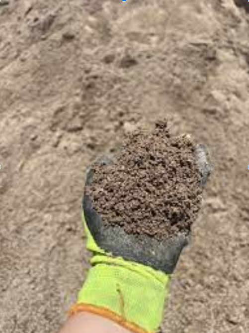 A person wearing a yellow glove is holding a pile of dirt in their hand.