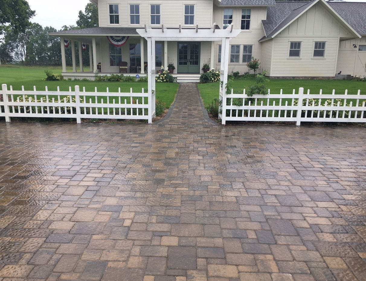 A house with a brick driveway and a white picket fence