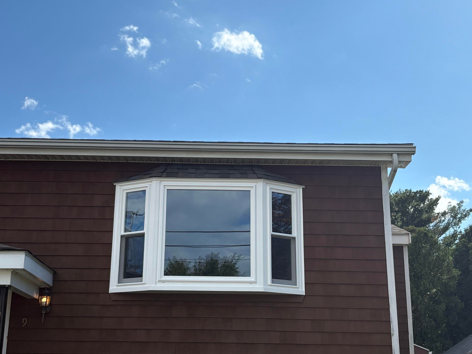 Brown house with a bay window, white trim, and a blue sky with clouds in the background.