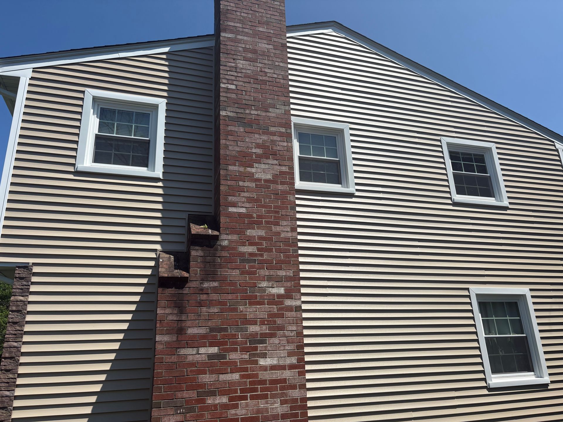 Tan-sided house with a red brick chimney and white-framed windows on a sunny day.