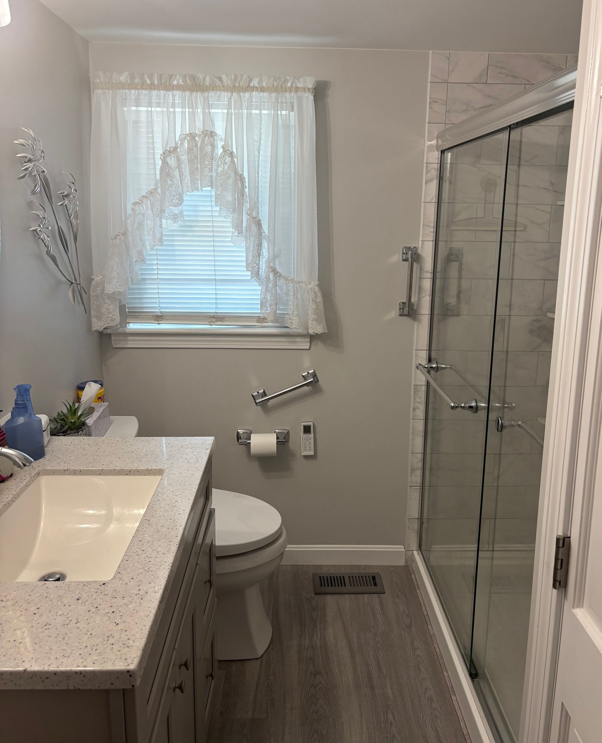 Bathroom with shower, sink, and toilet; light gray walls, white cabinets, and sheer curtains.