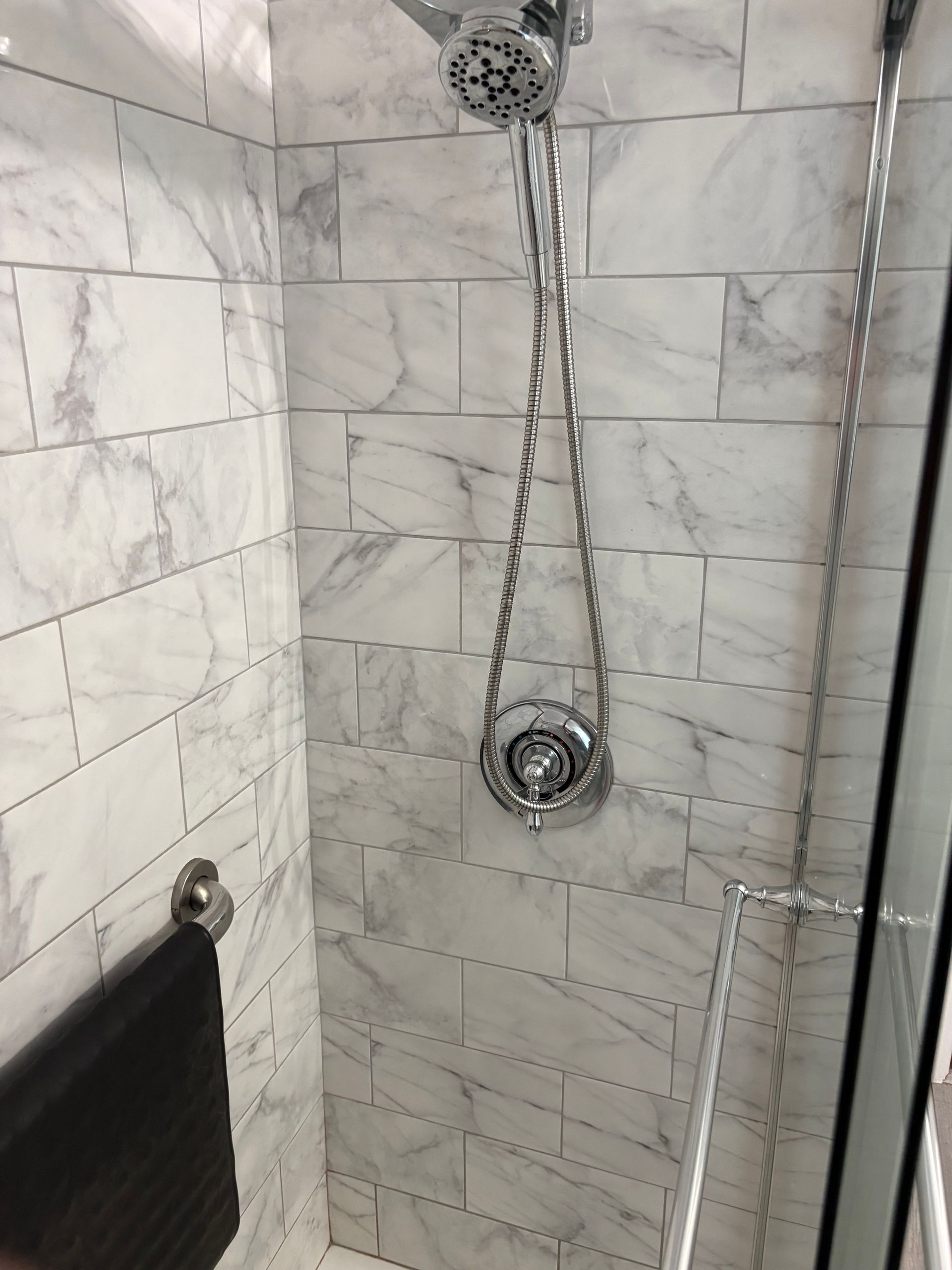 Shower stall with marble-look tiles, a chrome showerhead, and a towel on a bar.