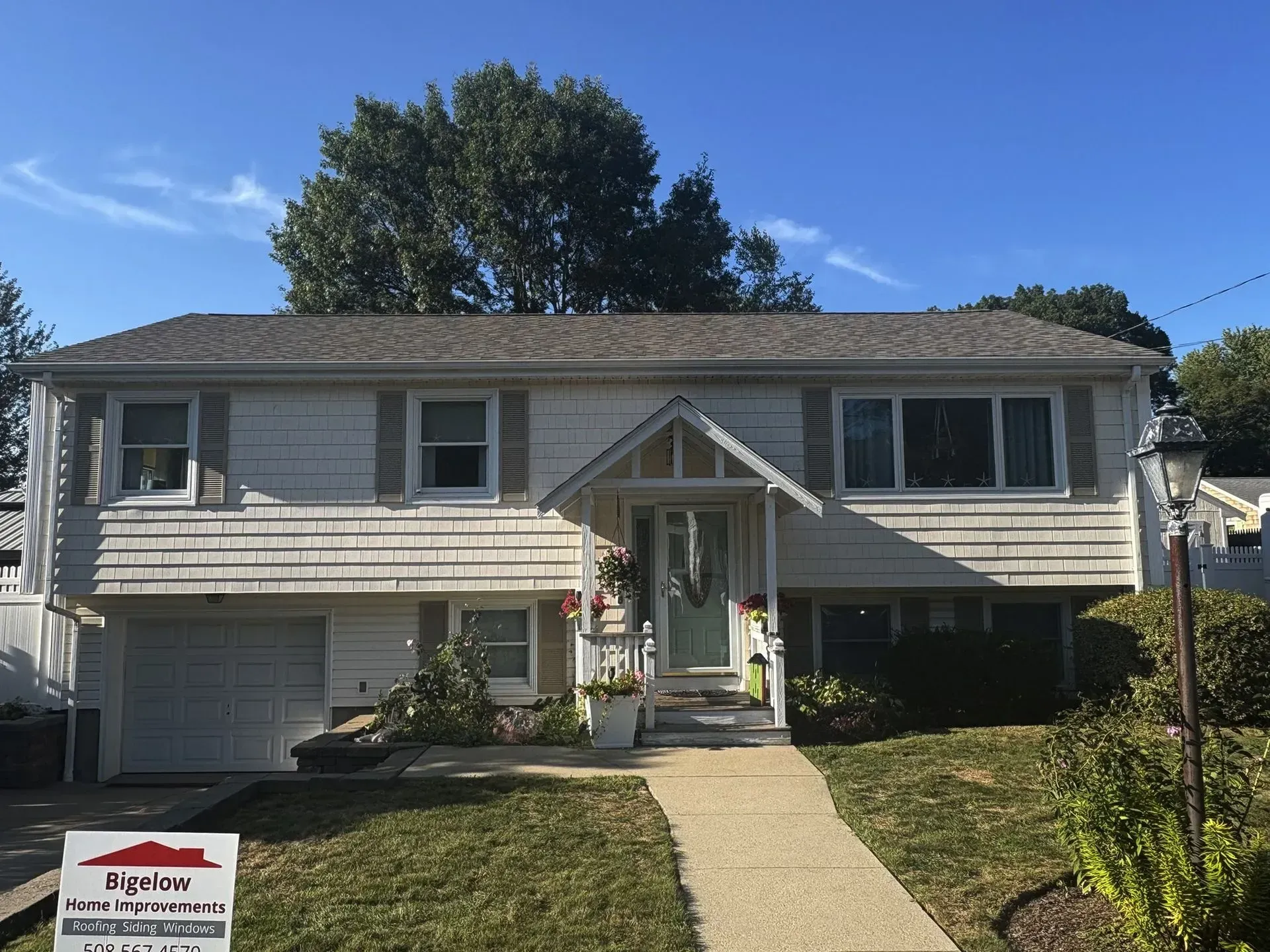 White house with a gray roof, small porch, and a concrete walkway on a sunny day.