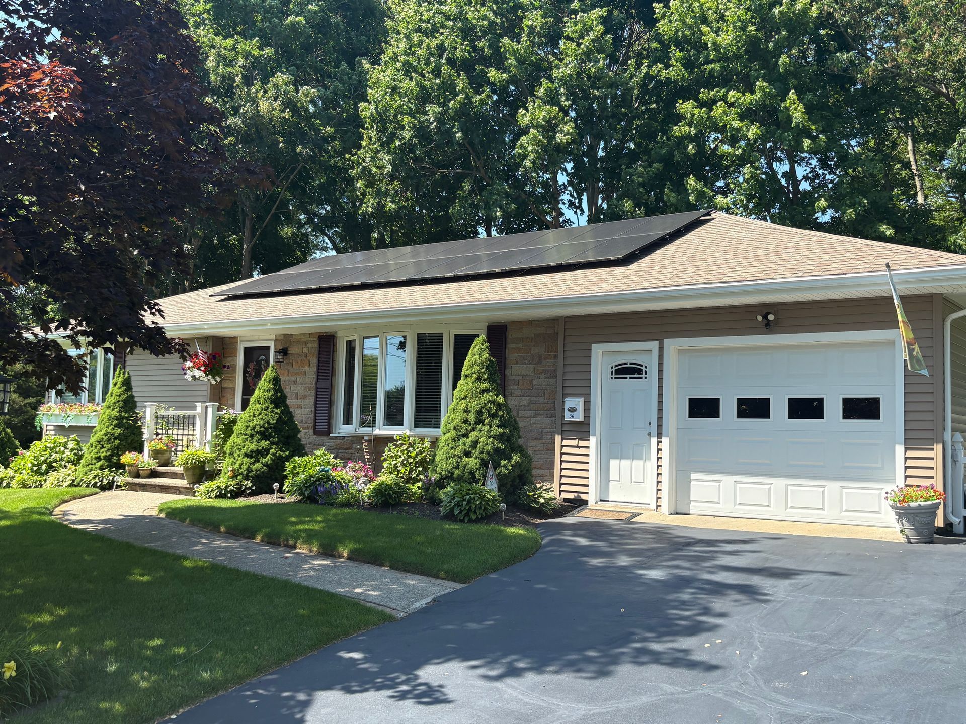 House with solar panels on roof, green lawn, brick facade, garage, and driveway. Sunny day.