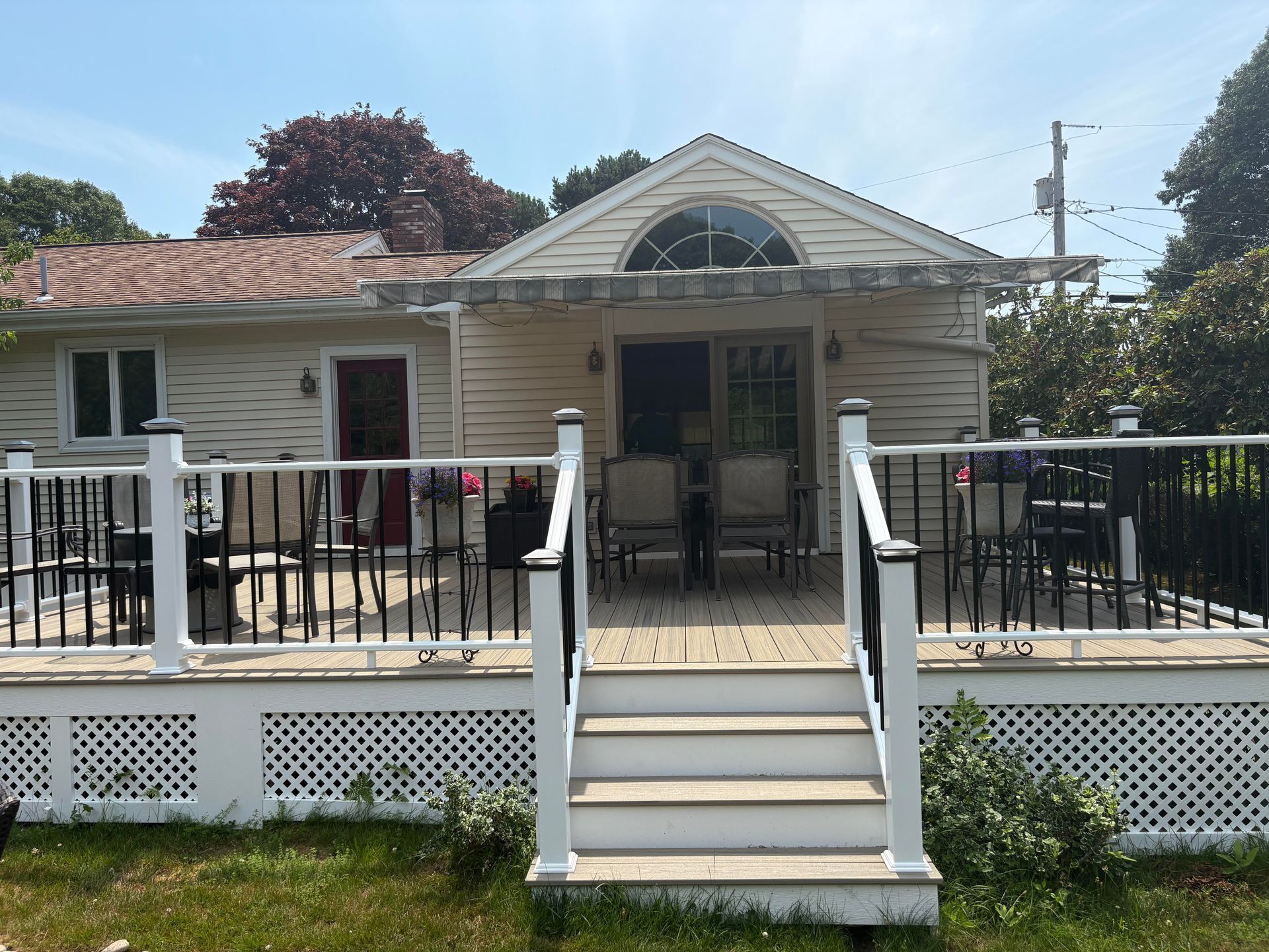 A house with a deck and steps, surrounded by a black and white fence and railings. Sunny day, blue sky.