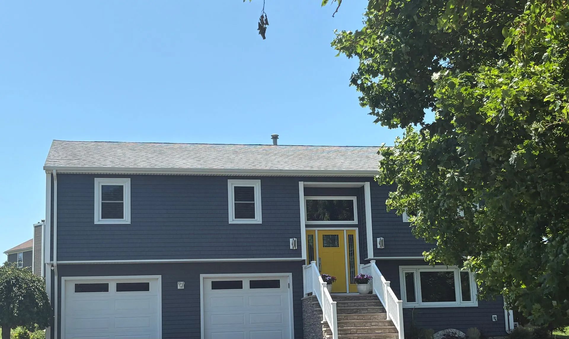 Blue house with white trim, yellow door, two-car garage, and tree in front of a blue sky.