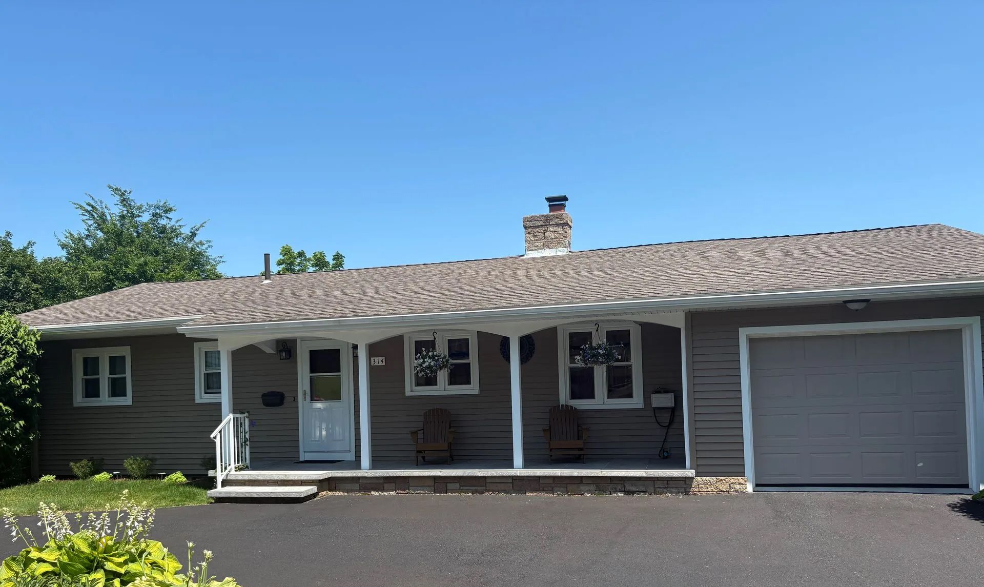 Gray ranch-style house with a covered porch, front door, and attached garage under a blue sky.