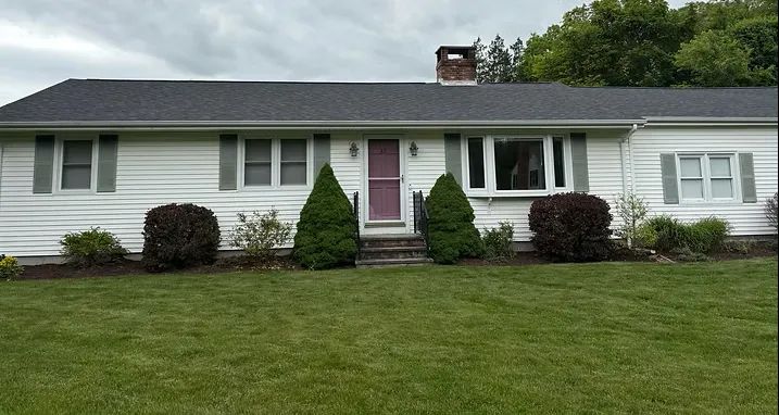 White ranch-style house with green lawn, shrubs, and a dark roof.
