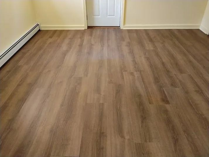 Room with wood-look flooring, beige walls, a white door, and a radiator.