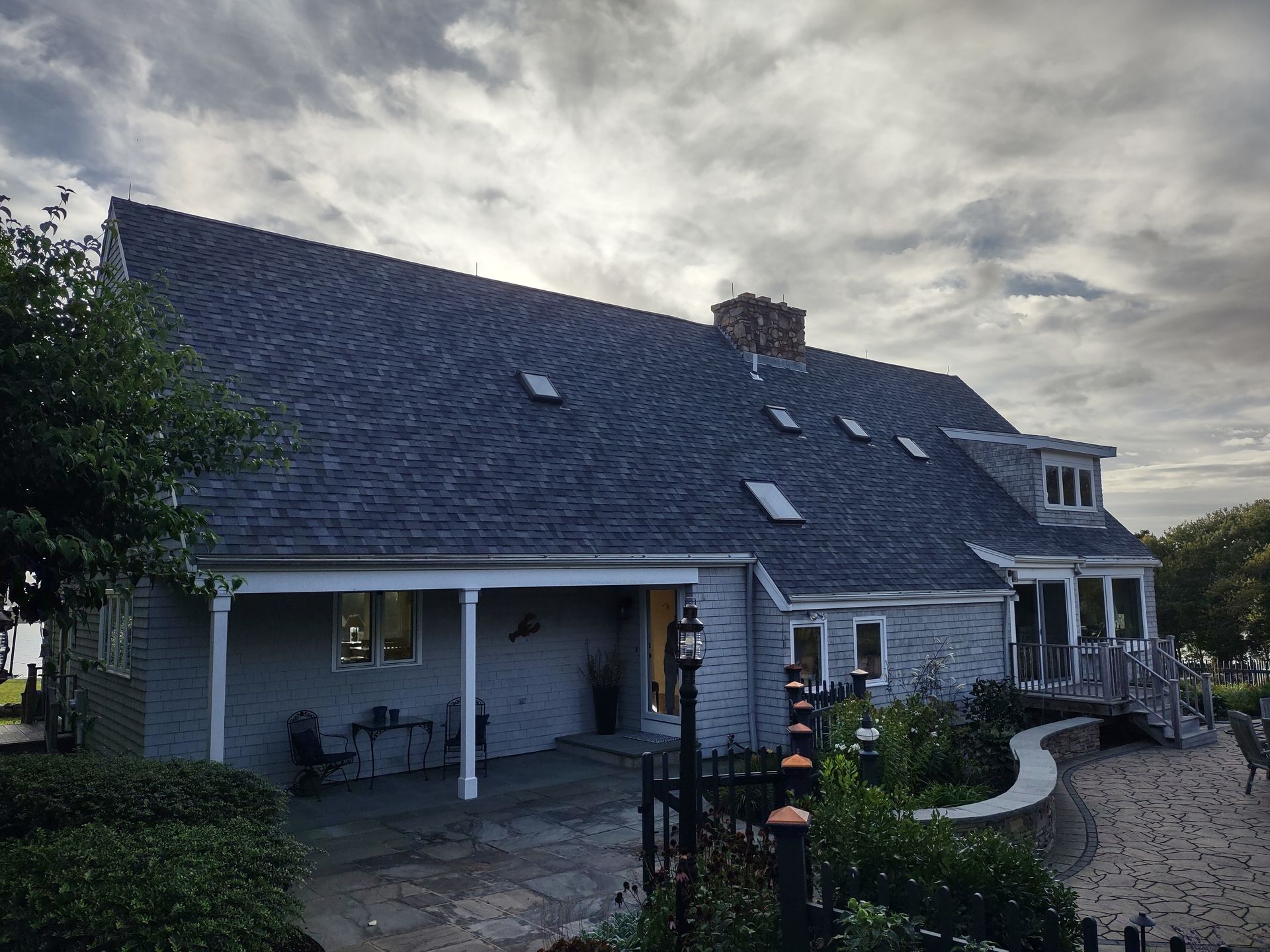 Gray house with a dark roof, covered porch, and small windows against a cloudy sky.