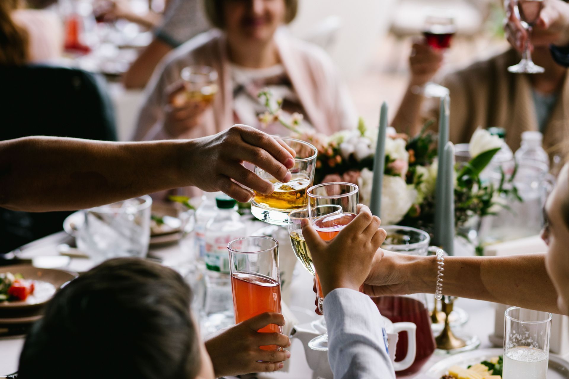 Hands clinking glasses at a festive dinner table with flowers and wine.